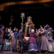 The Ghost of Christmas Present stands on a sleigh above a group of people in A Christmas Carol