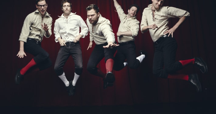 Five men in white shirts and black knickers are photographed in mid-air while jumping in front of a black background.