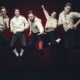 Five men in white shirts and black knickers are photographed in mid-air while jumping in front of a black background.
