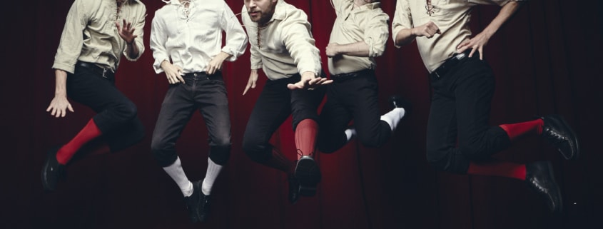 Five men in white shirts and black knickers are photographed in mid-air while jumping in front of a black background.