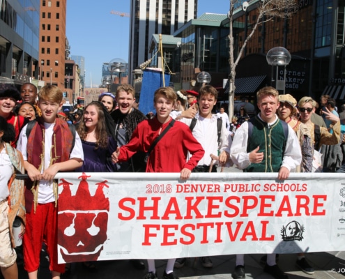 A group of Denver Public Schools students, dressed in Shakespearean costumes, hold a banner during a parade at the 2018 Shakespeare Festival