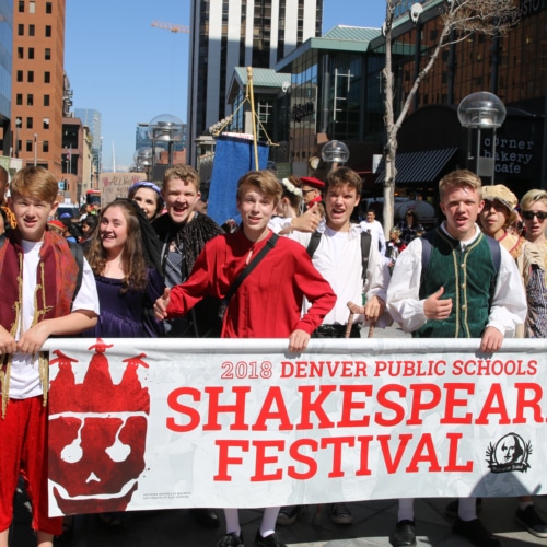 A group of Denver Public Schools students, dressed in Shakespearean costumes, hold a banner during a parade at the 2018 Shakespeare Festival