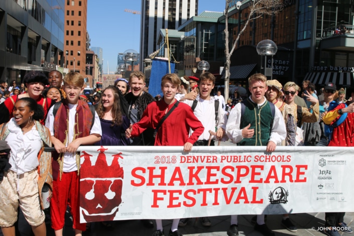 A group of Denver Public Schools students, dressed in Shakespearean costumes, hold a banner during a parade at the 2018 Shakespeare Festival