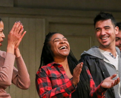 Four young adult actor stand in a row, smiling and clapping, at a DCPA Community Engagement event