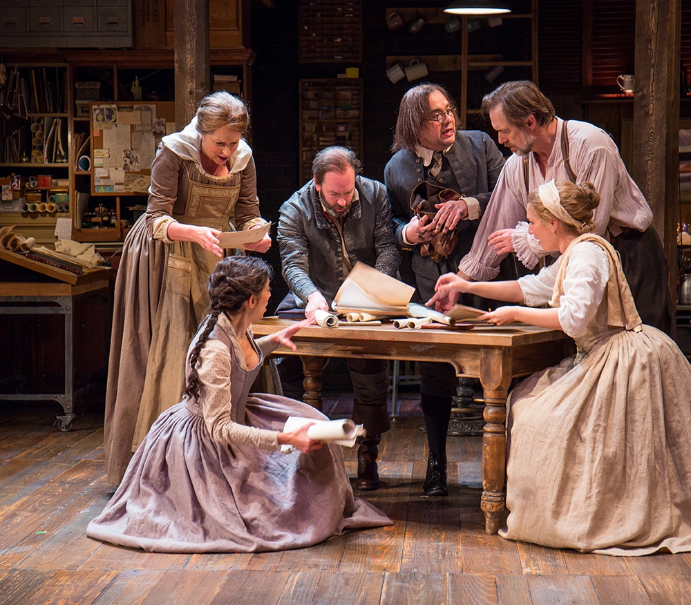 3 renaissance men and women in shock ad they gather around a wooden table with multiple scrolls spread throughout the table