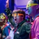 Audience members wearing bright-colored 3D glasses gasp in reaction to something out of frame