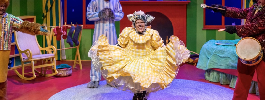 A brightly colored bedroom done in primary colors with an actor dressed as a bunny and an actress in the foreground dressed a furry animal curtsying in a yellow dress.