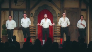 Five actors dressed in stockings, breeches, and billowy shirts stand onstage