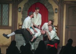 Four actors dressed in medieval garb surround another man who has fainted