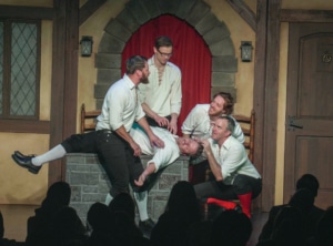 Four actors dressed in medieval garb surround another man who has fainted