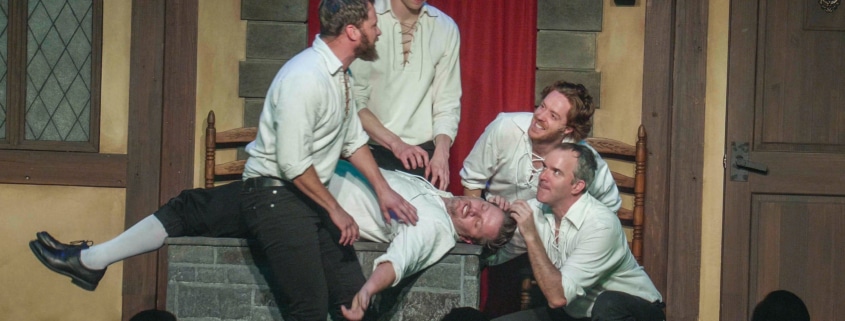 Four actors dressed in medieval garb surround another man who has fainted