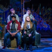 Four actors sit on stage looking out at the audience