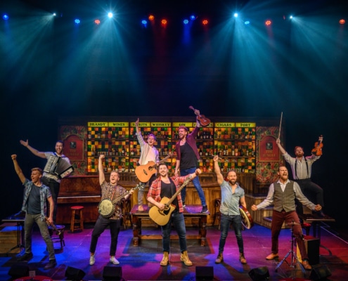 The nine primary cast members of The Choir of Man stand in formation with their musical instruments.