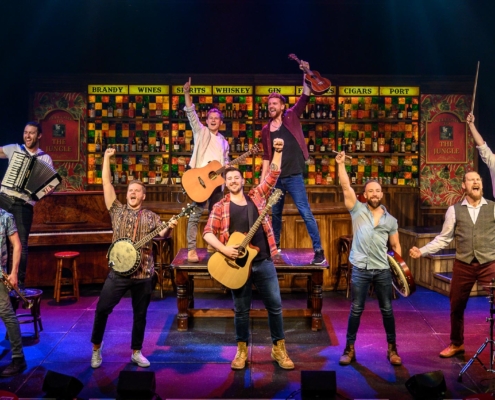 The nine primary cast members of The Choir of Man stand in formation with their musical instruments.