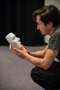 A man looks contemplatively at a white mask