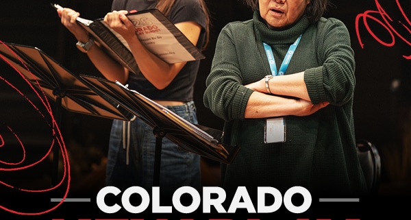 A graphic of two women rehearsing at the Colorado New Play Summit. One reads from a script, the other listens with arms crossed, conveying focus and collaboration. White and red text below reads "COLORADO NEW PLAY SUMMIT."
