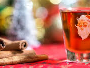 Raw cinnamon sticks arranged in a pile next to a Santa-themed shot glass filled with red liquid