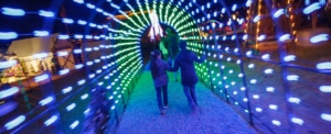 Camp Christmas. Two people walking through tunnel of lights with bright colors.