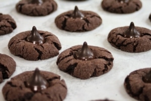 Peppermint blossom cookies topped with mint chocolate kisses aligned in rows on a baking sheet