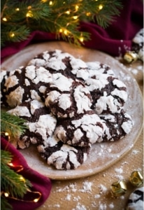 Chocolate crinkle cookies, garnished with powdered sugar, on a plate surrounded by Christmas decorations