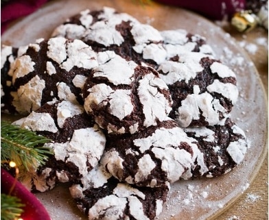 Chocolate crinkle cookies, garnished with powdered sugar, on a plate surrounded by Christmas decorations