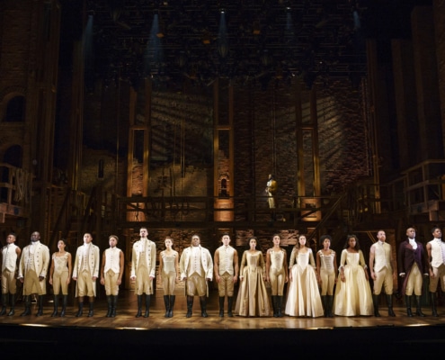 Cast of Hamilton Broadway National Tour stands in a line wearing all white and brown onstage