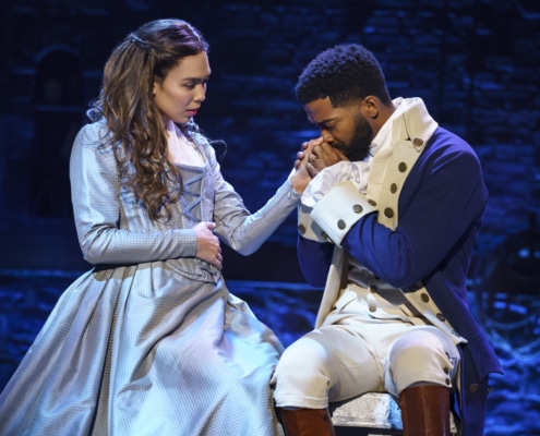 Elizabeth Schuyler sits next to Alexander Hamilton as he kisses her hand onstage in Hamilton Broadway National Tour