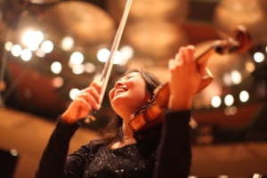 a woman looks up smiling with her violin tucked under her chin and the bow in her hand