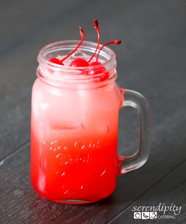 a red beverage in a mason jar style glass with cherries sticking out of the top