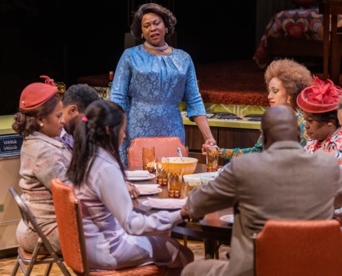 Chavez Ravine stands at the head of a table and prays with the cast of In the Upper Room, all dressed in their Sunday best