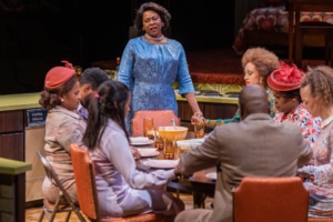 Actors hold hands sitting around a dinner table to pray onstage in In the Upper Room.