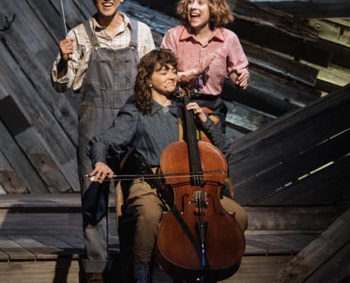 Esteban Suero and Alyse Alan Louis stand and sing behind Neyla Pekarek, seated and playing her cello, during a performance of Rattlesnake Kate