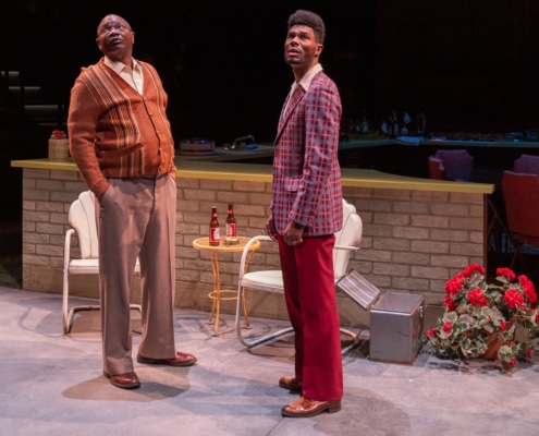 Levy Lee Simon and Matthew Hancock stand, facing each other, on a set designed to look like a front porch. They both look upward.