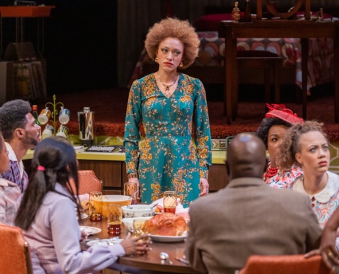 An actor stands at a dinner table where other actors are seated in In the Upper Room.