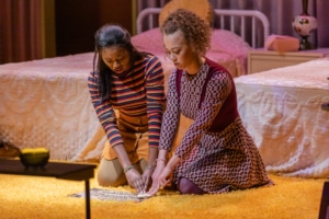 Two young actors sit on the floor holding their fingers on a Ouija board in In the Upper Room.