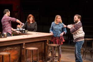 Actors stand around a bar in The Nest