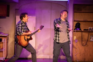 Seth Dhonau plays guitar while Brett Ambler sings onstage