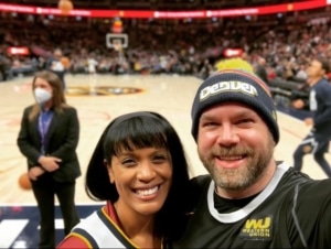 Nicole deBree smiles with her husband as they stand courtside at a Denver Nuggets game