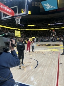 Nicole deBree stands on the court at a Denver Nuggets game with the mascot