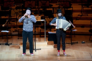 Two mimes perform, one holding an accordion and one playing a trumpet