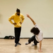 a dance teacher watches as a student executes a move on the floor