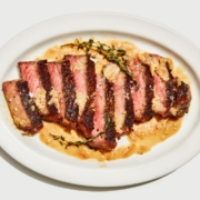 A seared steak cut into slices on a white tray