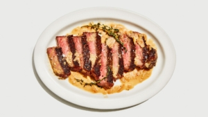 A seared steak cut into slices on a white tray