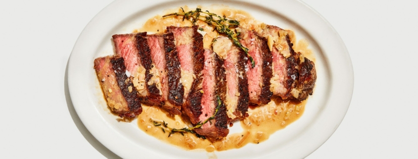 A seared steak cut into slices on a white tray