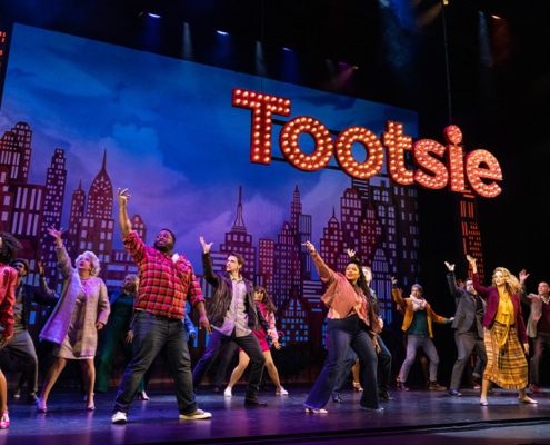 The cast of Tootsie pose onstage under a lighted 'Tootsie' sign