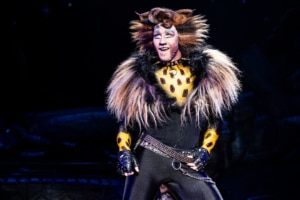 An actor dressed as a black spotted cat onstage in Cats