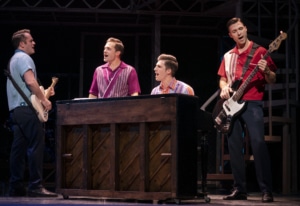 The members of The Four Seasons stand around a piano singing in Jersey Boys