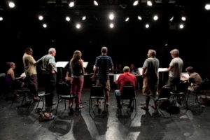 a row of actors reading scripts on a dark stage