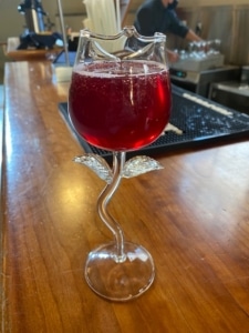 Red cocktail in rose shaped glass sitting on a bar