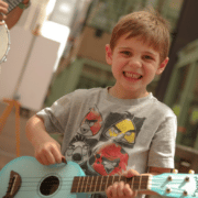 A child smiles while holding a small blue guitar